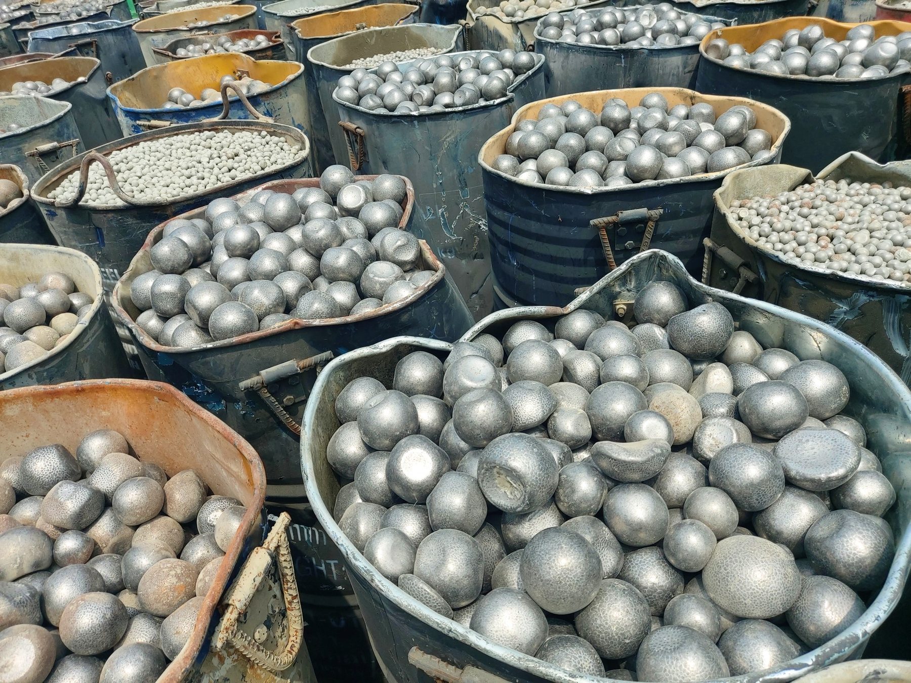 Used grinding media balls of different sizes stored in industrial drums